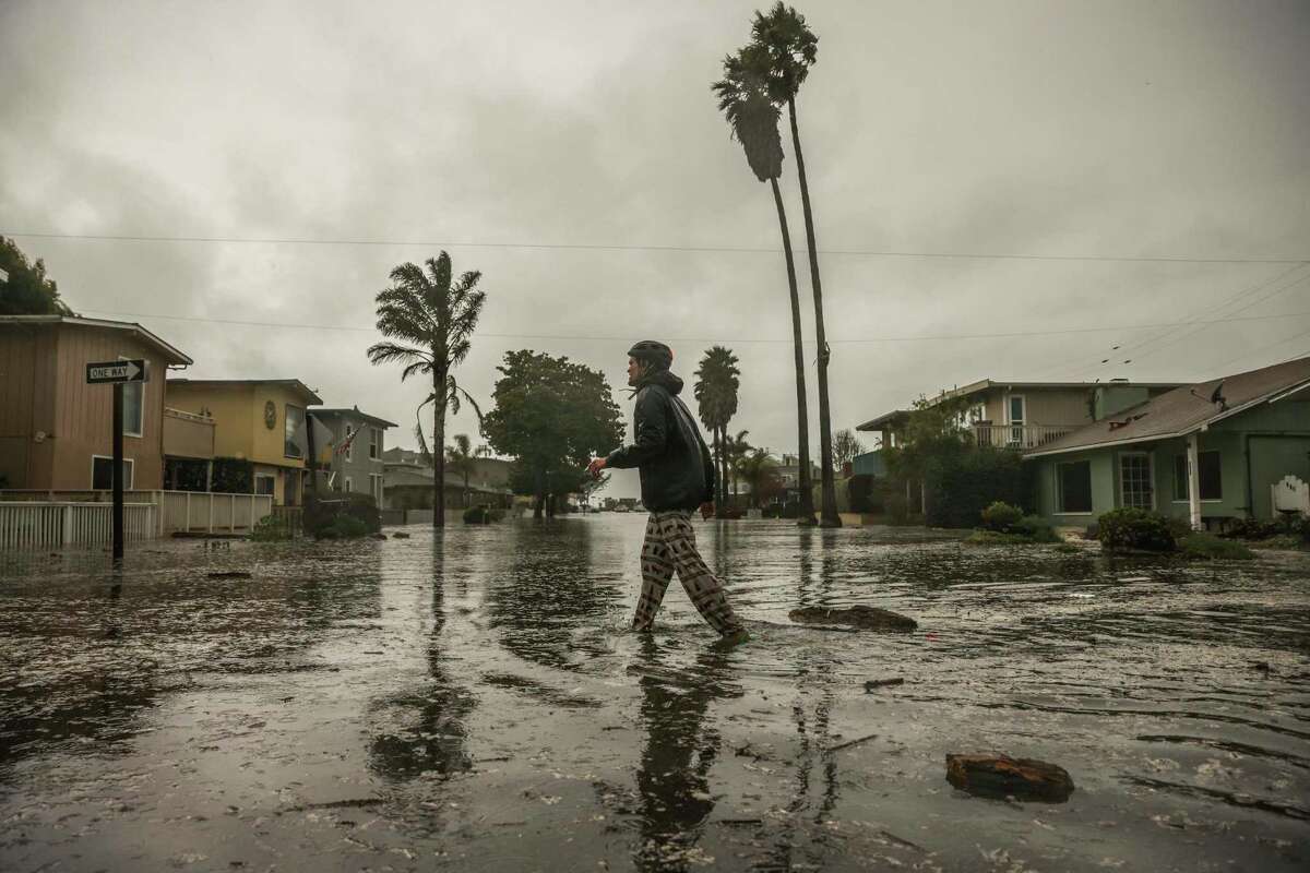 在圣克鲁斯县阿普托斯海滩大道上，迈克·帕内罗涉水帮助被风暴淹没的邻居。
