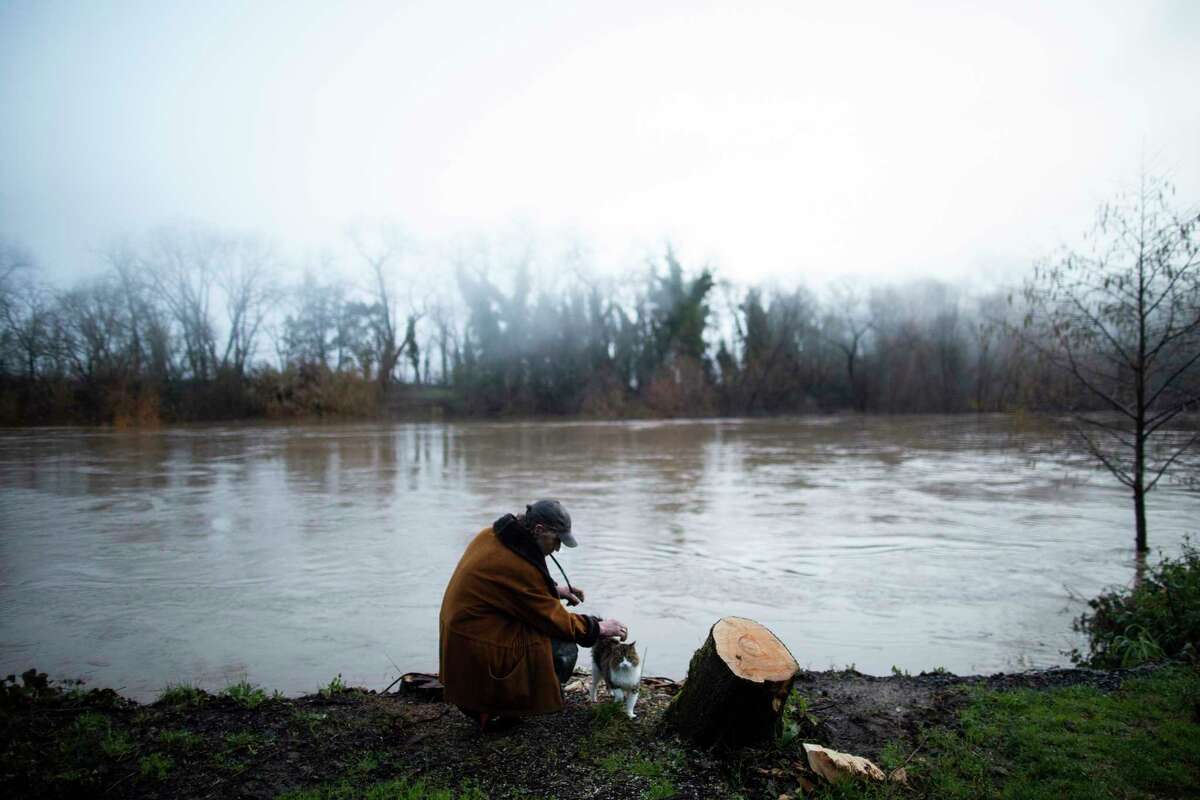 Jerry Monticello pets his cat and watches the Russian River rise at his home in Forestville on Sunday.