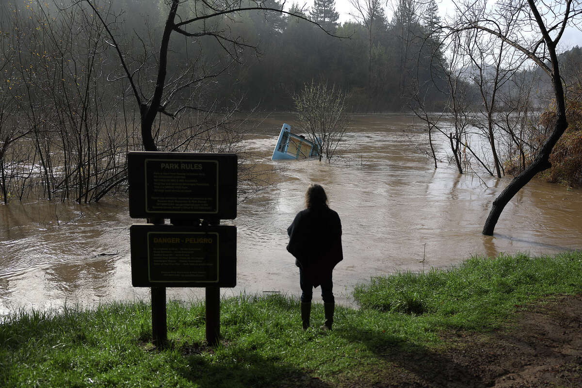 A resident looks at a boat that is caught in a tree in the Russian River on Jan. 9, 2023, in Rio Nido, Calif.