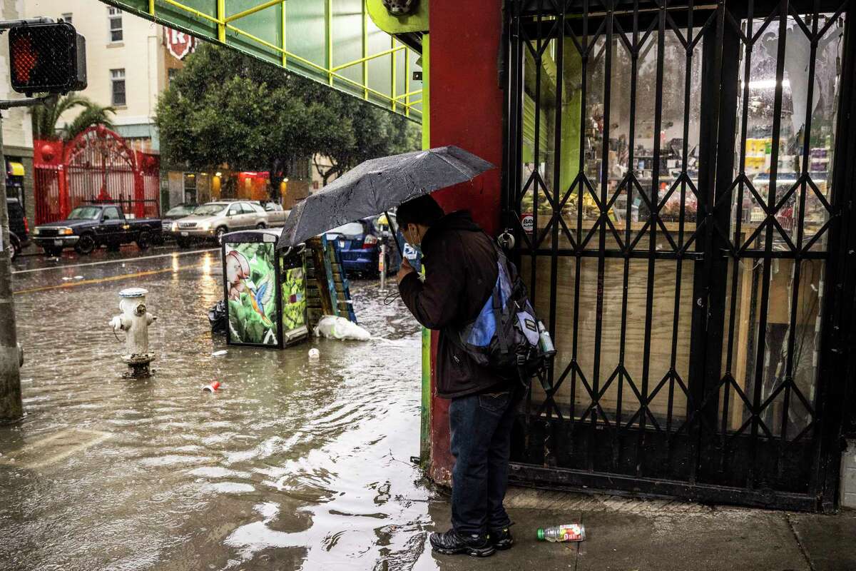 2023年1月10日星期二，加利福尼亚州旧金山，一名行人在埃利斯和莱文沃斯街的拐角处看着被洪水淹没的人行道。