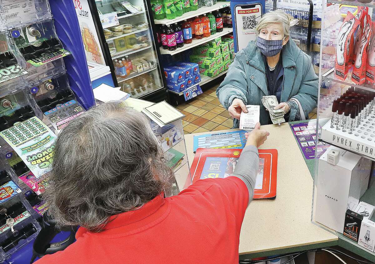 John Badman|The Telegraph Brown Street Shell clerk Bernadette Bridges, foreground, hands what could be a winning ticket to a customer Thursday for the $1.35 Billion Mega Millions drawing Friday night.