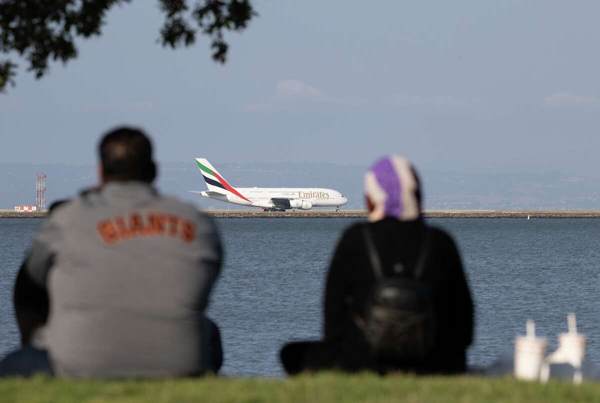 A couple watches as an Emirates Airlines plane prepares to take off at SFO in September 2022.