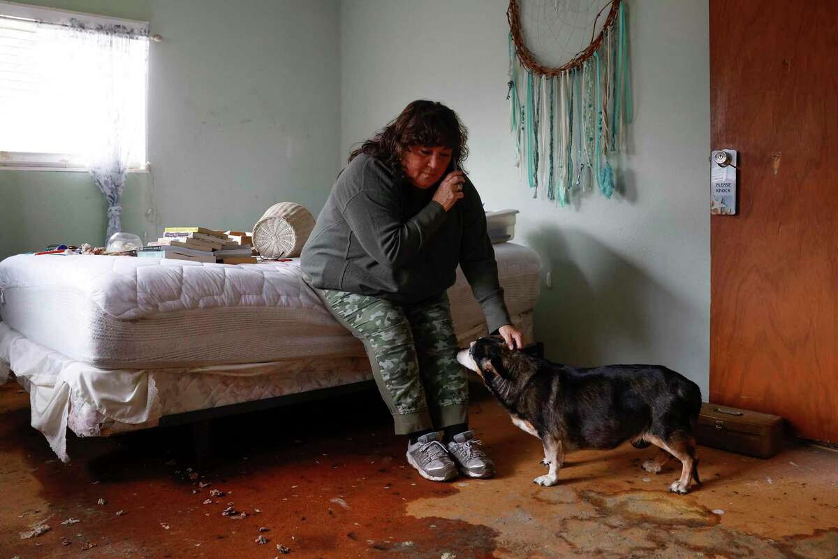 Photographer Jessica Christian’s mother, Victoria Christian, talks on the phone with her landlord while petting her 16-year-old dog, Sheba, in her flooded bedroom in Sunol.