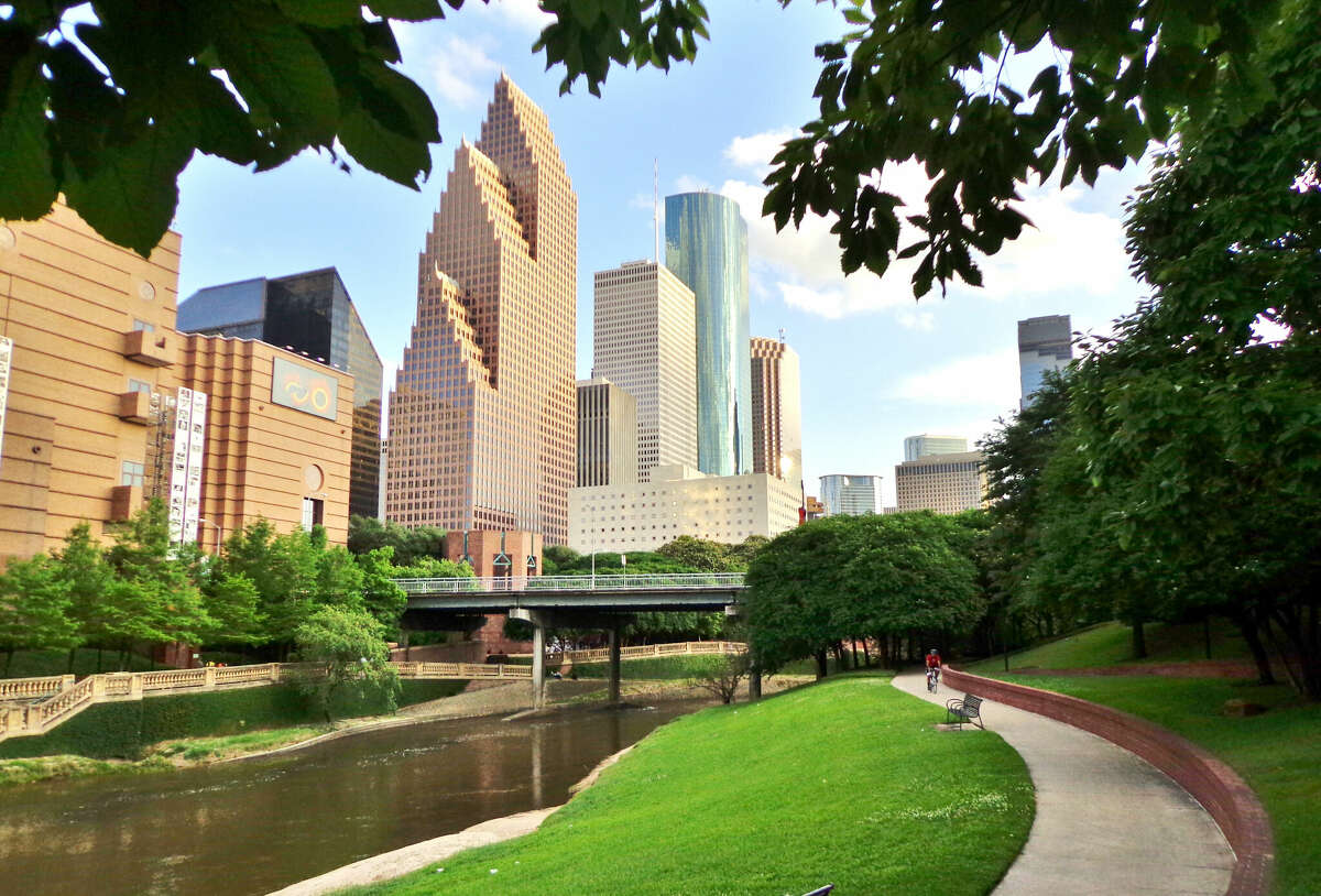 Wide shot of Houston's skyline and paved bike/walkway in Buffalo Bayou Park on a summer afternoon.