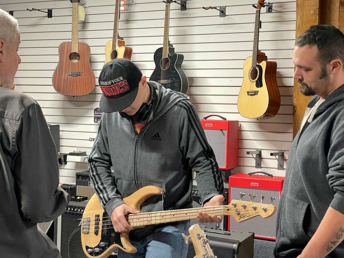 Customer Rebel Freiberg (center) tries out a bass guitar at Quinn's Music alongside his father, Dan (right), and owner Marc Conley.