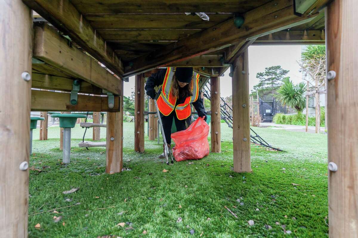 Community member and volunteer Rosemarie Sims picks up trash under a playground in the Hunters View neighborhood of San Francisco on Sunday.