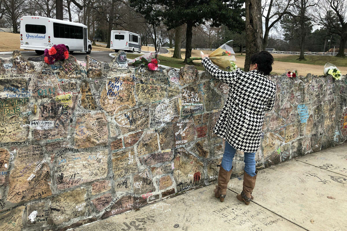 A fan places a bouquet of flowers on the stone wall outside Graceland on Friday, Jan. 13, in Memphis, Tenn. Lisa Marie Presley will be buried at Graceland, her father Elvis' mansion that on Friday was a gathering place for fans who were distraught over the singer-songwriter's death. A memorial ceremony is planned at Graceland on Jan. 22.