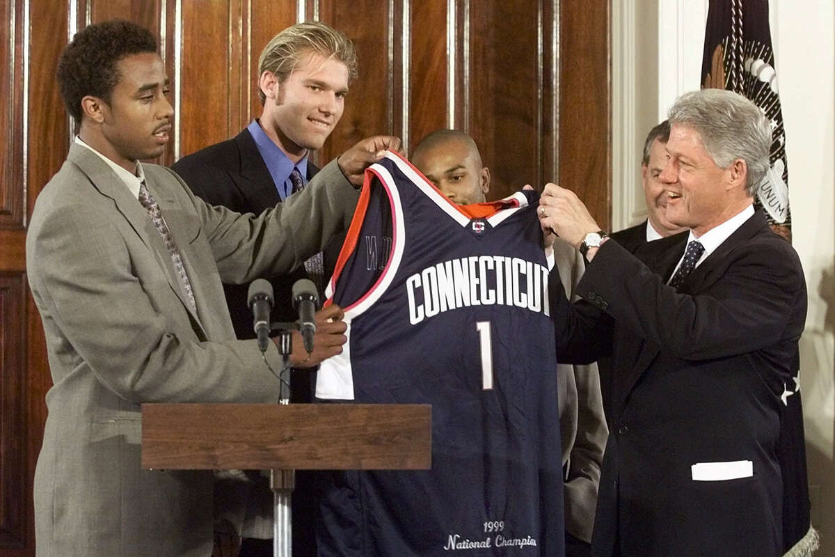 President Clinton receives a commemorative jersey presented by University of Connecticut basketball players from left Kevin Freeman, Jake Voskuhl, Ricky Moore and UCONN Coach Jim Calhoun during a ceremony honoring the team at the White House Thursday, Oct. 14, 1999. UCONN beat a heavily favored Duke team to win the NCAA National Championship last spring.