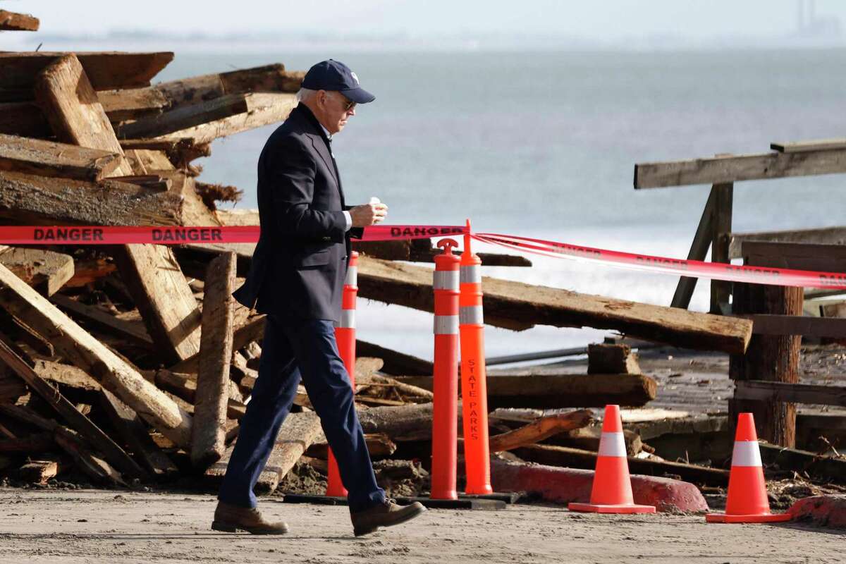 拜登总统走过阿普托斯海崖州立海滩废墟码头附近的海岸线上堆积的成堆的木头。
