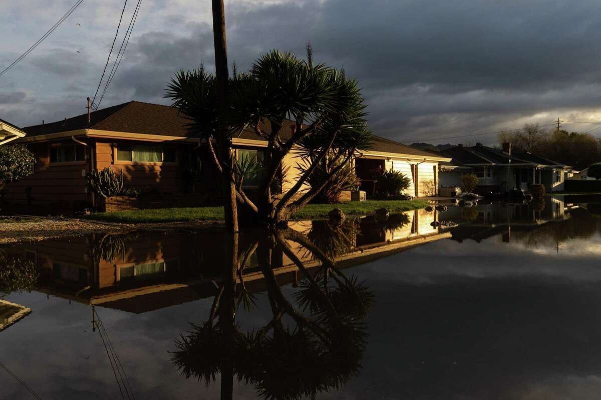周一，早晨的阳光照射在沃森维尔拉肯大道上一所被洪水淹没的疏散房屋上。未来袭击加州的风暴可能会变得更加猛烈。
