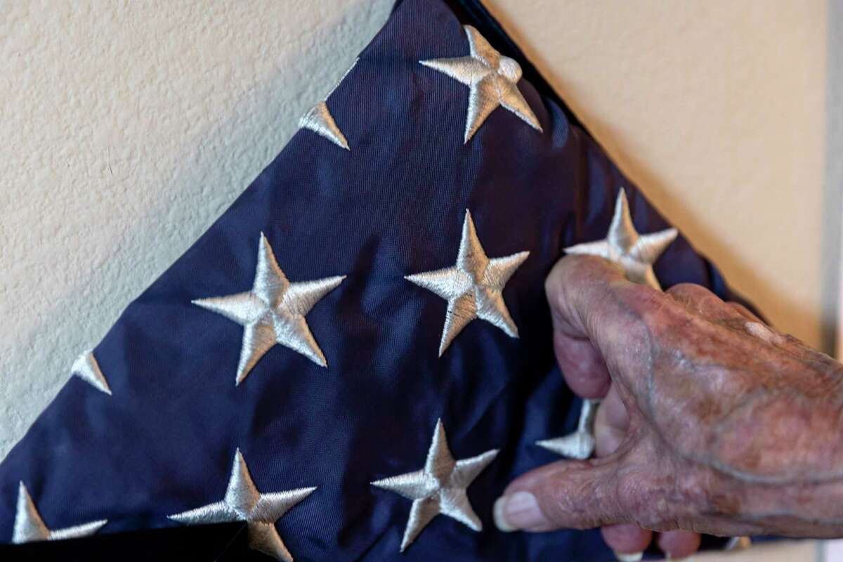 Army Staff Sgt. Bennett Stampes gently touches an American flag flown in Belgium over the graves of American soldiers that was raised and lowered by Stampes is seen in his home in San Antonio on Jan. 12.