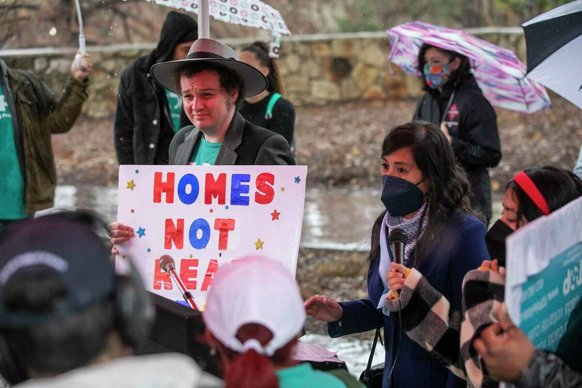Ashton Condel of the Texas Organizing Project holds a sign reading “homes not realty” as Councilwoman Adriana Rocha Garcia speaks during a press conference held at Labor Plaza in downtown San Antonio, Texas, on Jan. 24, 2023. Community groups and local leaders came together in calling for the City of San Antonio to develop and pass a citywide resolution that promotes existing rights tenants have, while reaffirming the city’s commitment to just housing practices. The efforts to adopt a Tennant Bill of Rights is based on the belief that no matter one’s age, race, physical ability, income level, or ZIP code, all San Antonians deserve safe and stable housing.