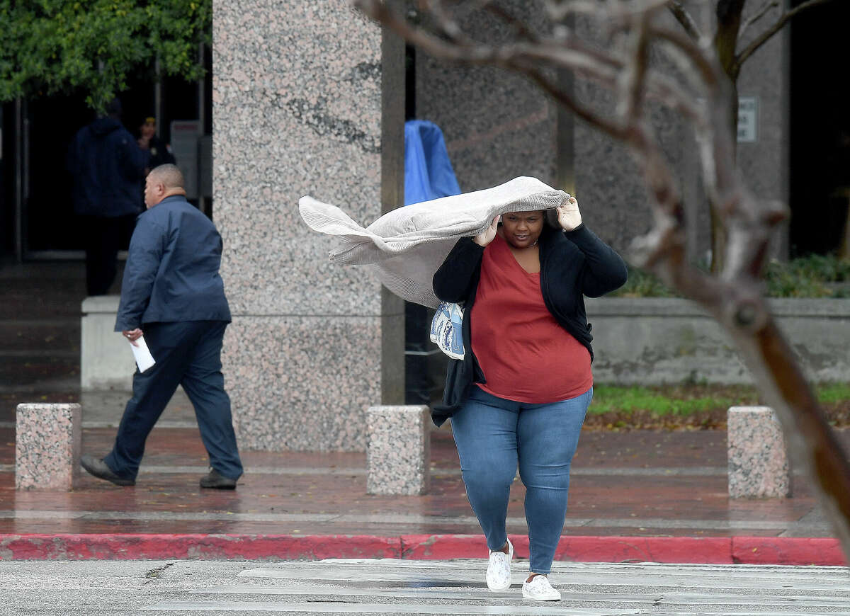 A woman uses a sweater after her umbrella failed in gusting winds while leaving the Jefferson County Courthouse, which closed as heavy storms with high winds moved through the region Tuesday afternoon. Photo made Tuesday, January 24, 2023 Kim Brent/Beaumont Enterprise