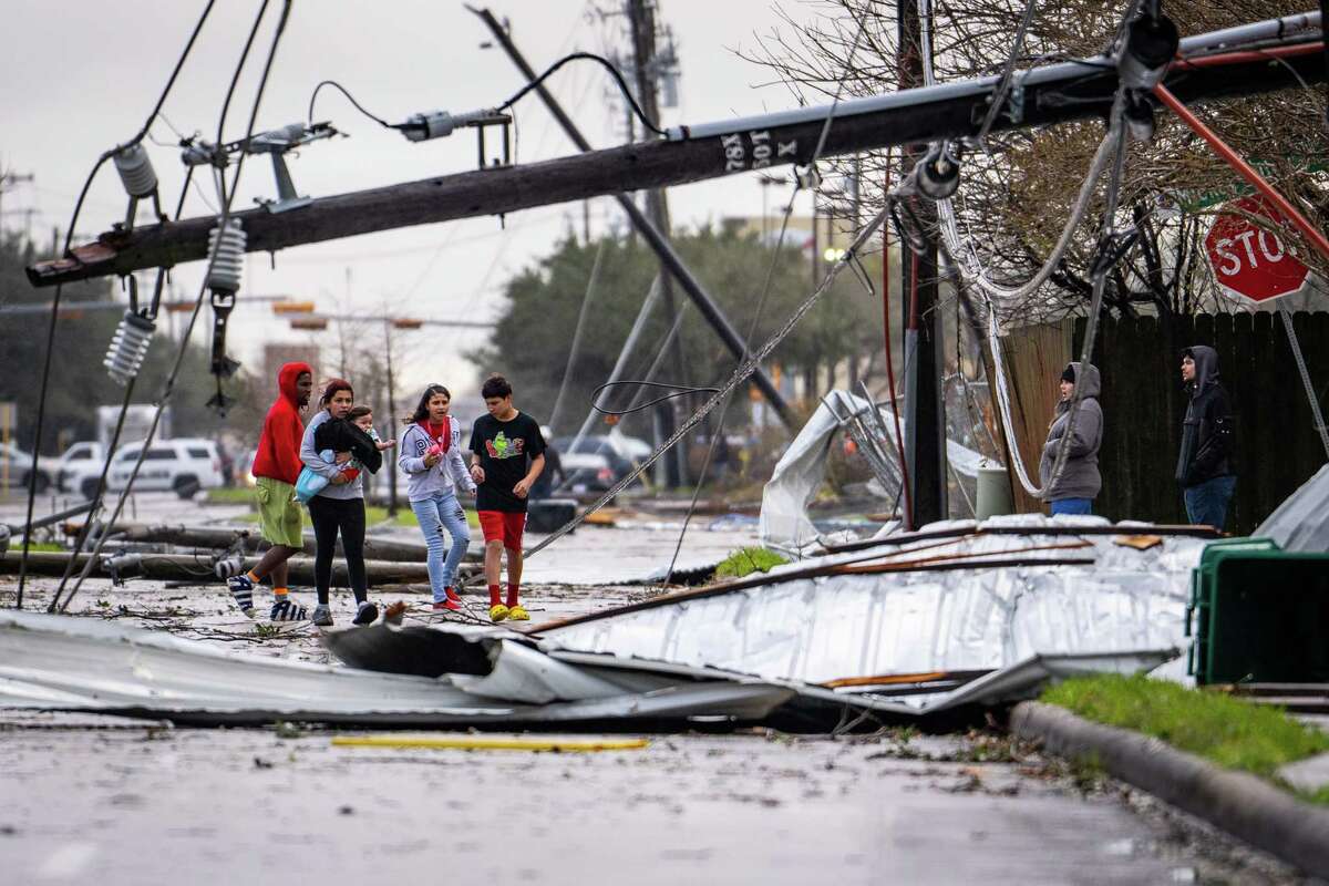 People cross under downed power lines where a tornado was reported to pass along Mickey Gilley Boulevard near Fairmont Parkway, Tuesday, Jan. 24, 2023, in Pasadena.