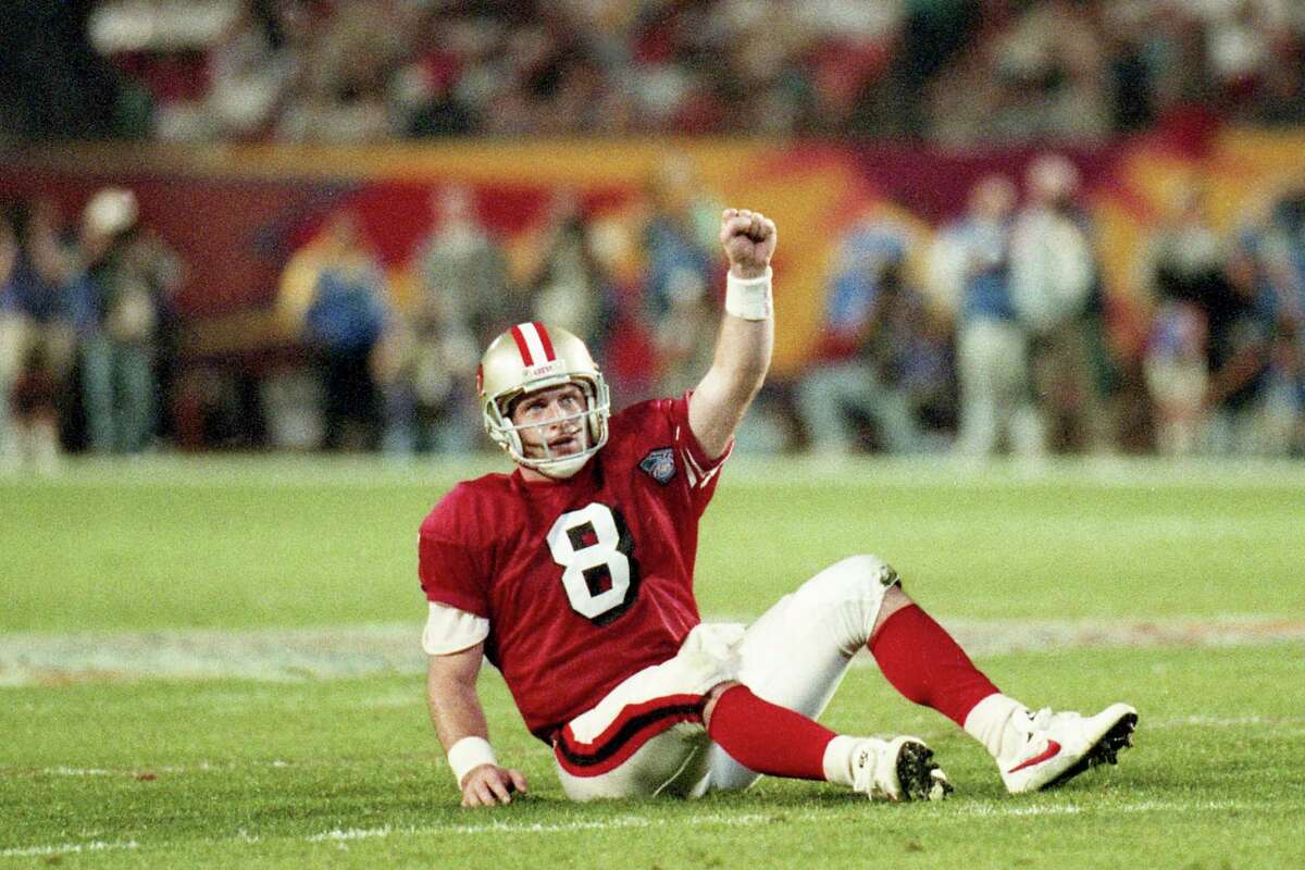 Steve Young sits on the field with his arm raised in triumph after throwing for a touchdown in the 49ers 1995 Super Bowl win over the San Diego Chargers.