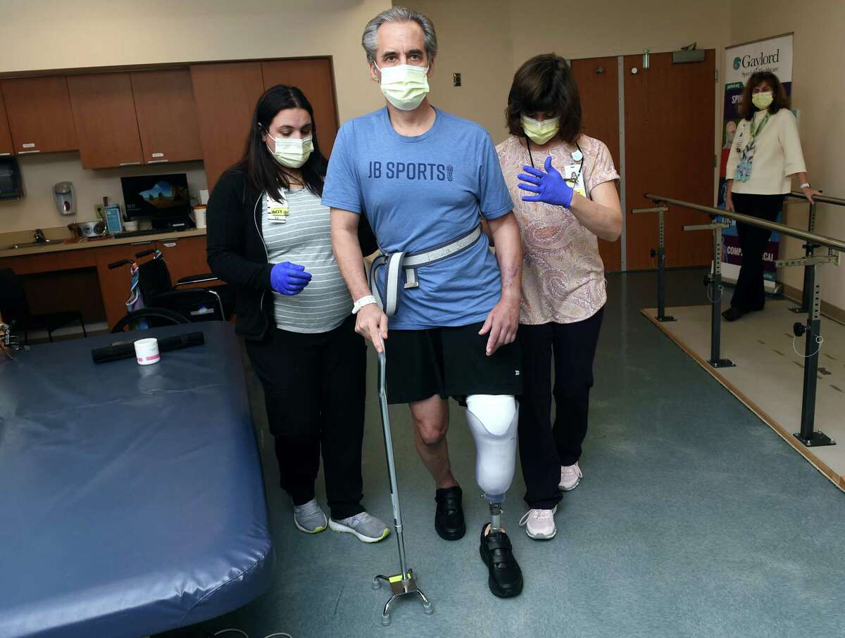 Runner and cyclist John Bysiewicz walks using a cane with the asssitance of Occupational Therapist Jaclyn Lavigne, left, and Physical Therapist Paula Savino to increase balance and mobility at Gaylord Hospital in Wallingford.