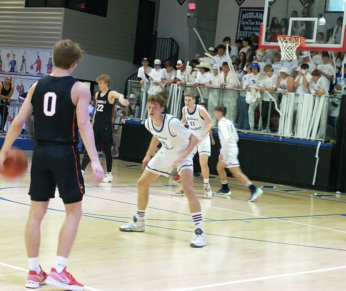 Midland Christian's Zach Day looks to guard Fort Worth Christian's Bobby Gutierrez (0) as loud and rowdy MCS student section cheers in the background at McGraw Event Center. 