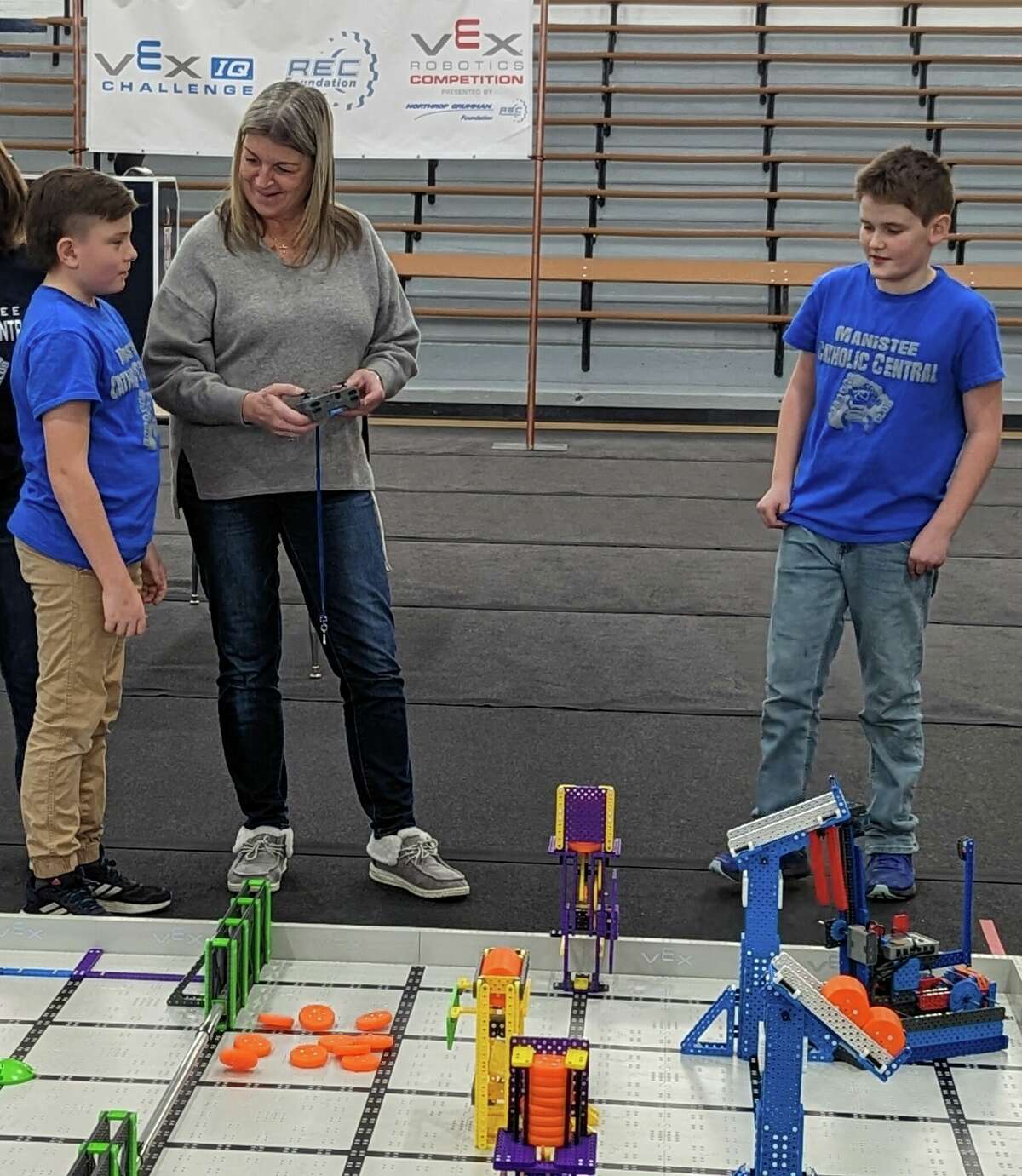 Manistee Catholic Central students, Easton Pierce and Liam Gentz show principal Catherine Grinn how to drive their robot at a robotics competition held on Jan. 28.