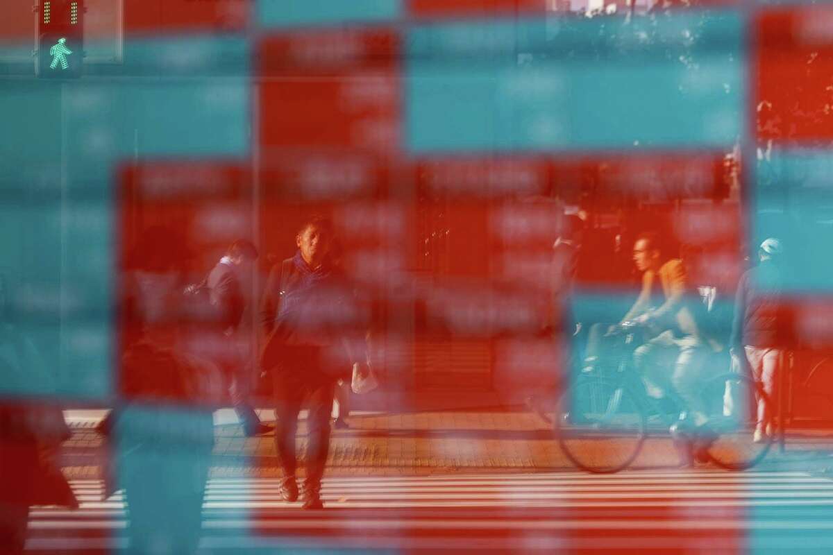 Pedestrians are reflected on an electronic stock board outside a securities firm in Tokyo, Japan, on Monday, Nov. 21, 2022. The world's central banks must keep raising interest rates to fight soaring and pervasive inflation, even as the global economy sinks into a significant slowdown, the OECD said.