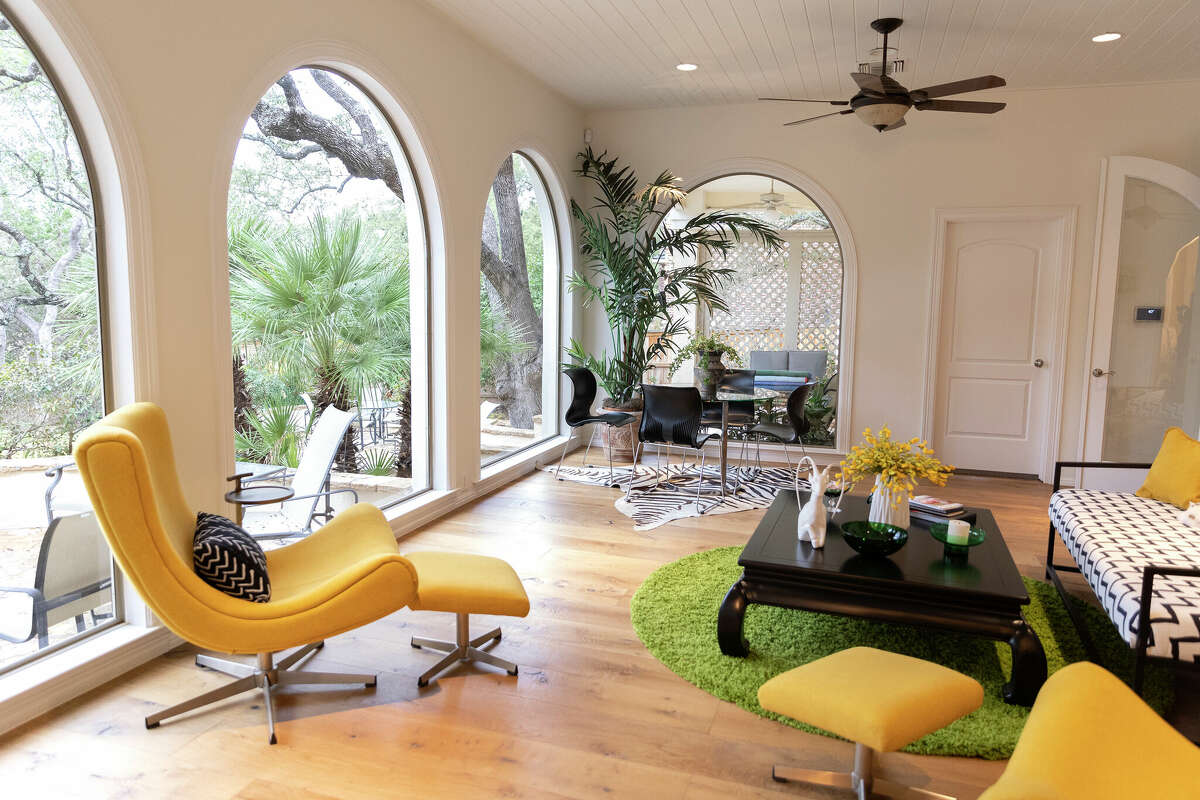 The sunroom is playfully furnished with a pair of scooped, midcentury mustard chairs and matching ottomans, a black-and-white, zig-zag-patterned love seat and a faux zebra throw rug.