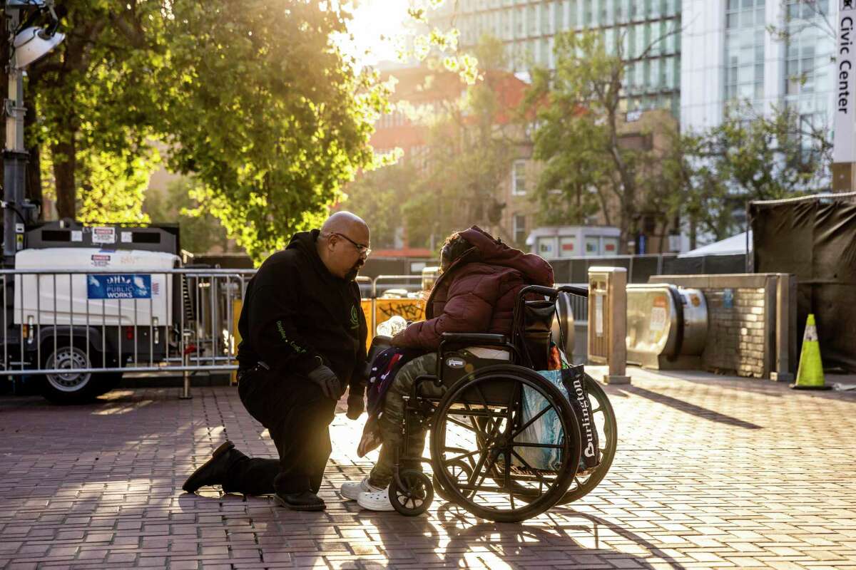 Louie Hammonds, Director of Acquisitions, Talent and Training at Urban Alchemy, talks to a distressed person on a wheelchair as they wait for a coffee after the person was found amidst vehicle traffic on Market Street in San Francisco, Calif. Tuesday, April 12, 2022. The city has tapped Urban Alchemy to run a pilot program to respond to low-level 911 calls about homelessness instead of police.