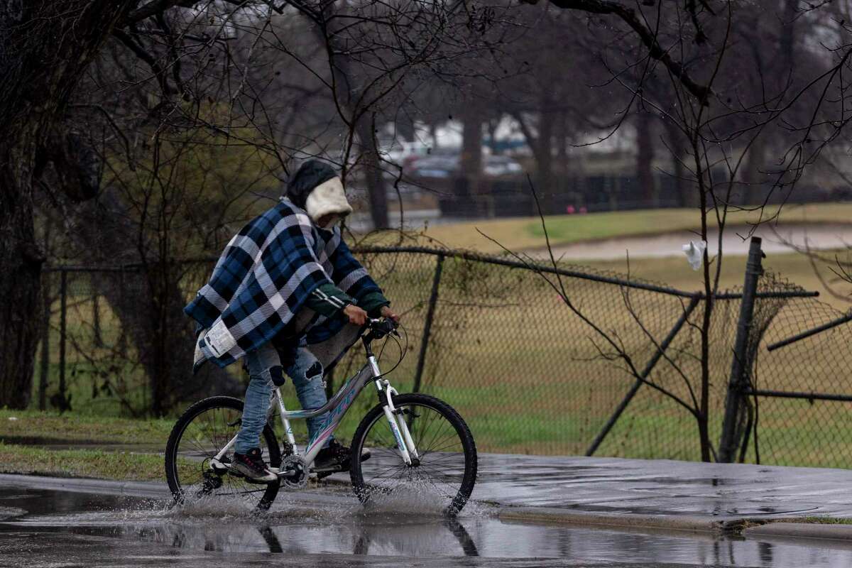 A man wears a blanket like a cape as he bikes through puddles on Wednesday. With the worst of the ice storm over, many San Antonio school districts are headed back to class Thursday. Though a few area districts are altering class times.