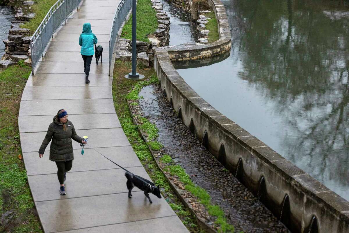 Bundled up pedestrians walk their dogs on along the San Antonio River near the Bluestar Art Complex in San Antonio, Texas, on Feb. 1, 2023. A strong cold front blew through the area lowering temperatures into the low 30’s with ice accumulations and power outages.