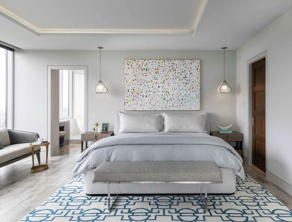 The primary bedroom is filled with light from the floor to ceiling windows, and the couple gets a bit of color in new artwork and a rug with a blue geometric pattern. 