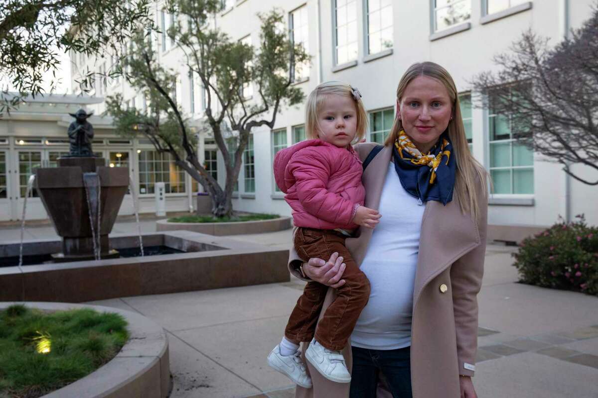 阿纳斯塔西娅·诺沃日洛娃(Anastasia Novozhilova)抱着两岁的女儿艾达(Ada)，站在旧金山一栋大楼的入口处，这里是她女儿的日托和学前班Bright Horizons Letterman数字艺术儿童保育中心。