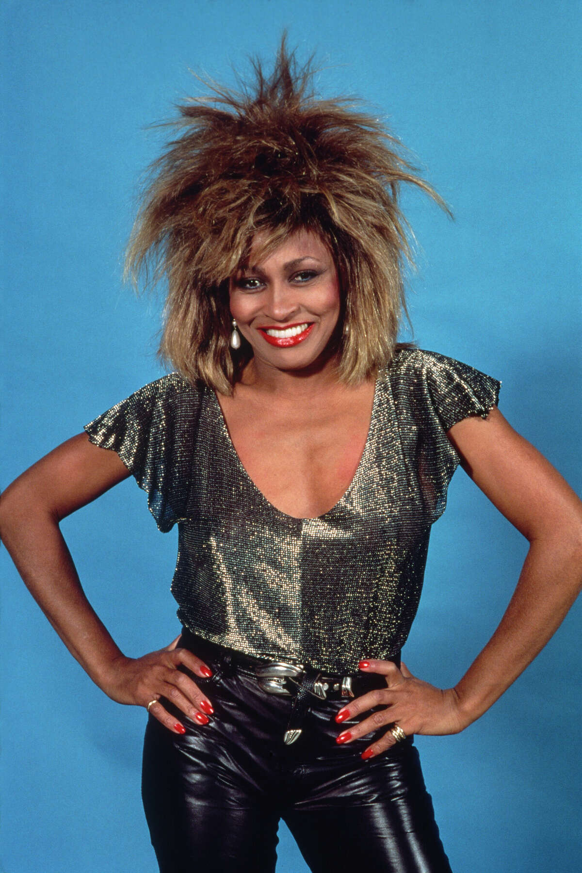 Tina Turner poses during a photoshoot. She is wearing a sparkling top with an '80s style haircut.