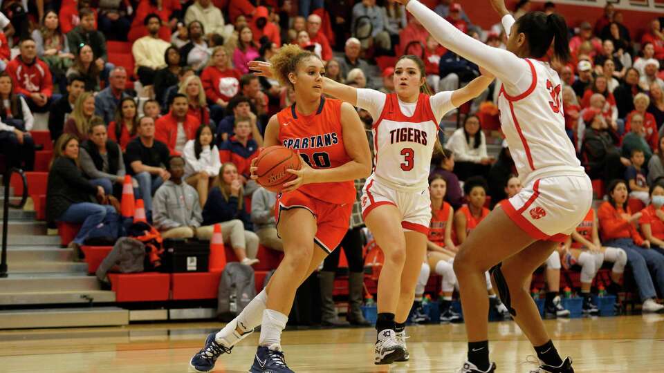 Seven Lakes Spartans Justice Carlton (30) drives to the basket while defended by Katy Tigers forward Lyric Barr (30) and Nyla Wold (3) during the high school basketball game between the Seven Lakes Spartans and the Katy Tigers at Katy High School in Katy, TX on Friday, February 3, 2023. The Seven Lakes Spartans defeated the Katy Tigers.