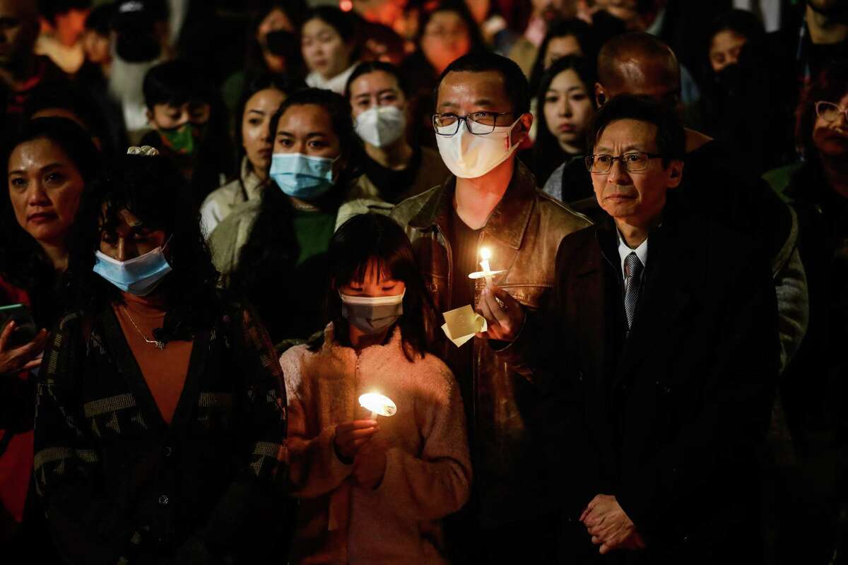 Leto Sze, 9, and father Michael Sze hold candles last month as they listen during the AAPI Unite candlelight vigil honoring the victims of the Monterey Park, Half Moon Bay and East Oakland shootings in Oakland.