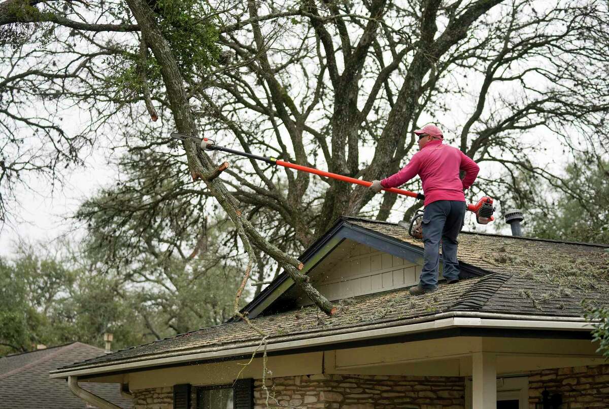 Eric Garcia removes a fallen tree limb from the roof of a house on Far West Boulevard in Austin, Texas, on Monday, Feb. 6, 2023, after an ice storm last week. (Jay Janner/Austin American-Statesman via AP)