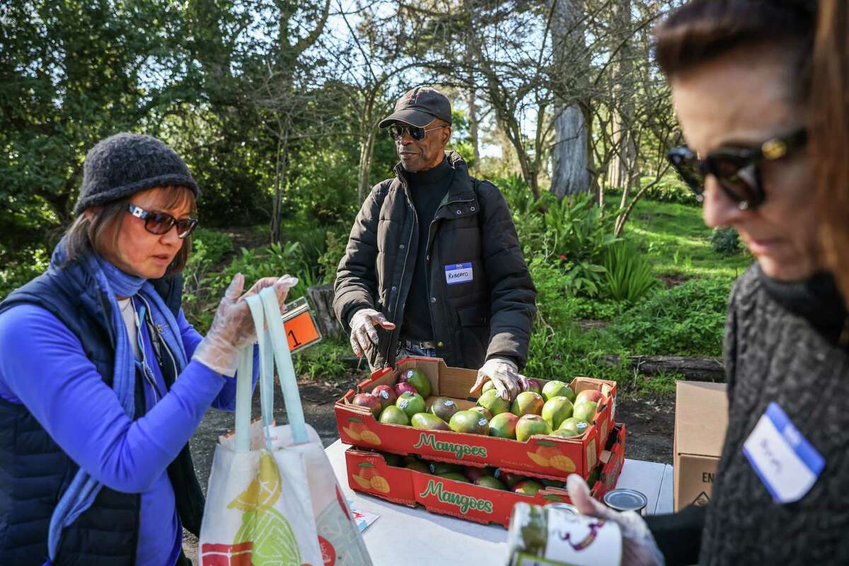志愿者罗伯托·奥萨维奥(中)和安·凯利(右)周一在旧金山外里士满的s.f.m arin食品银行的弹出式食品储藏室分发食物。