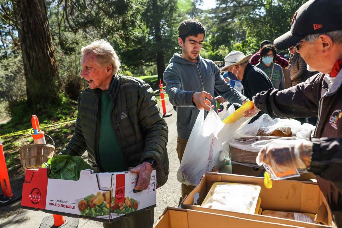 周一，德里克·斯基德莫尔(左)在外里士满的旧金山马林食品银行的弹出式食品储藏室里，一名男子(拒绝透露姓名)从汤姆·休伯纳(右)那里得到一箱农产品。