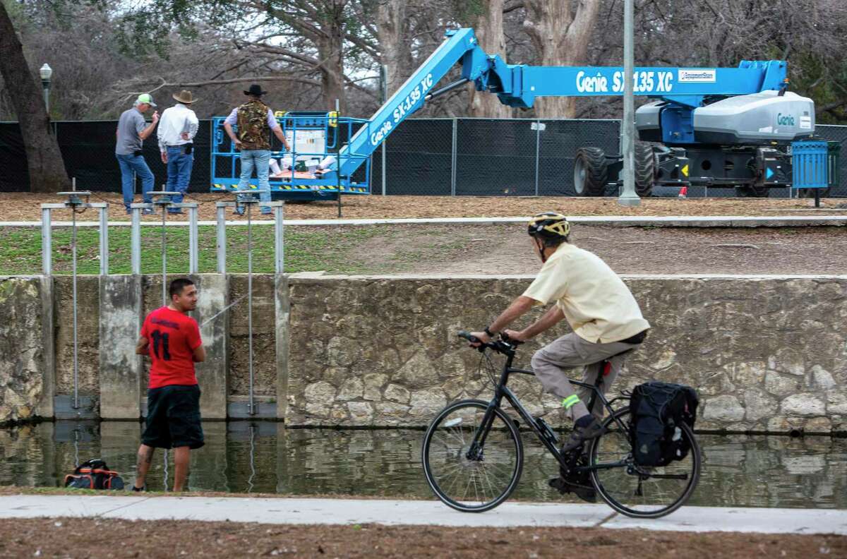 People use one side of the river in Brackenridge Park Tuesday, Feb. 7, 2023, as workers in the background use equipment on the other side of the river to harass egrets and herons nesting in the park near Joske Pavilion. The federally protected, migratory birds have nested in the park for at least two decades but their concentrations have grown so much in recent years they are causing environmental impacts to the San Antonio River water quality, according to the San Antonio Parks and Recreation Department.