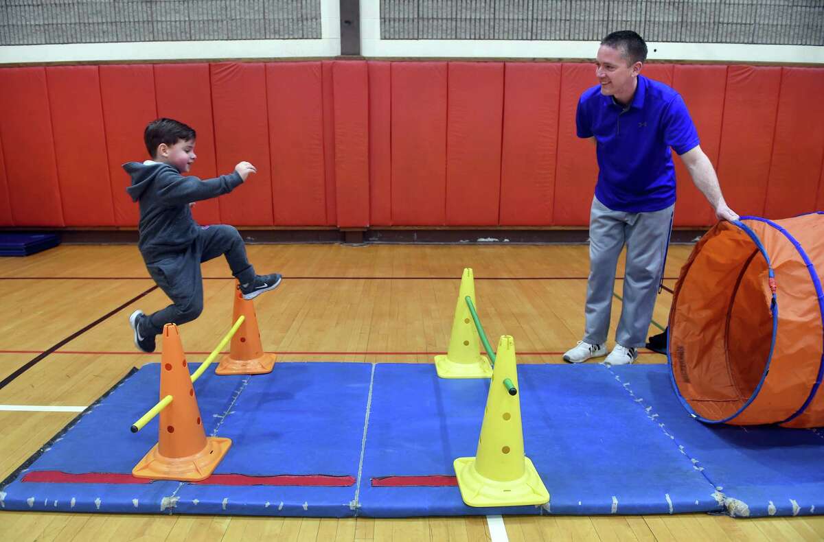 Physical education teacher Glenn Healy watches kindergartner Lucas D'Amato jump over a bar in an obstacle course in the gymnasium at Savin Rock Community School in West Haven.