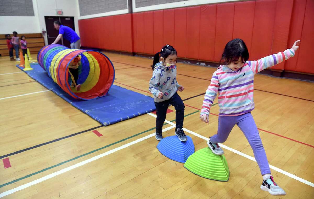 Kindergartners Lina Gong, center, and Jasmine Baoudene, right, make their way through an obstacle course in the gymnasium at Savin Rock Community School in West Haven.