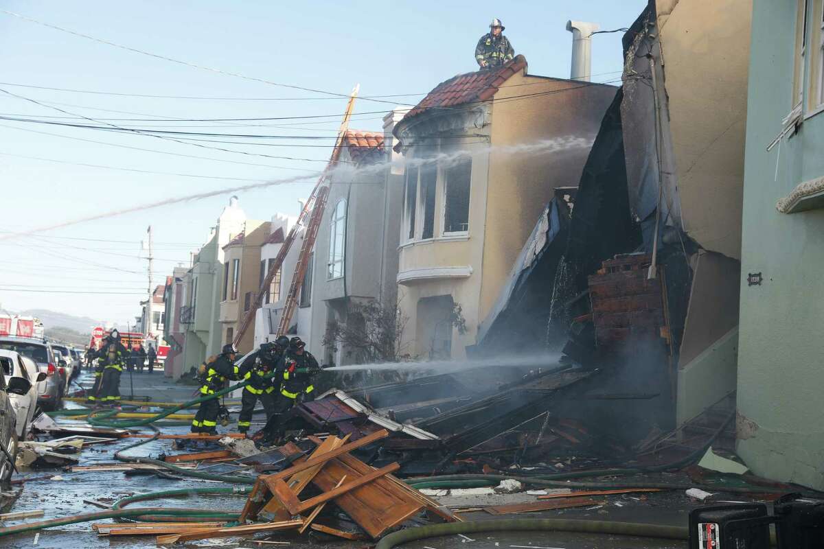 Firefighters use a hose to spray water on a home on 22nd Avenue at a third-alarm fire on Thursday in San Francisco.