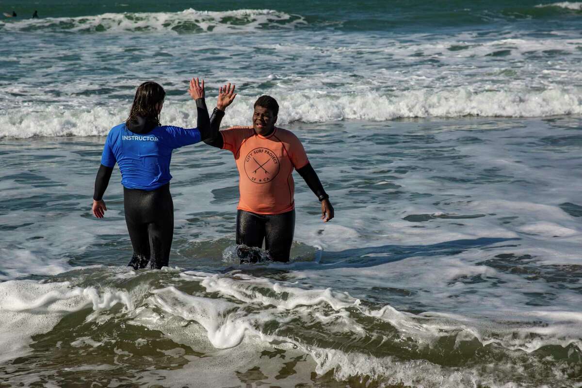 Damiane Fisher, 16 (right), a surf club student from Mission High School in San Francisco, high-fives City Surf Project instructor Andrew Perry after an afternoon of surfing at Linda Mar Beach in Pacifica.
