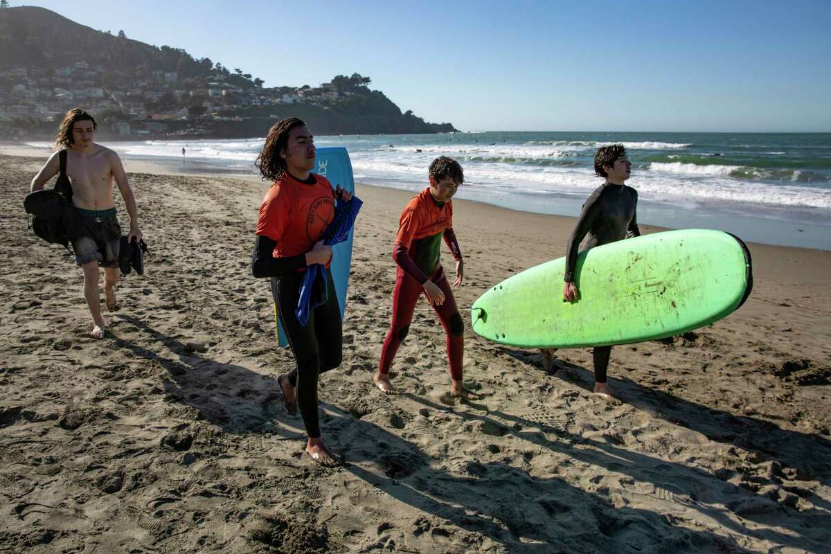 冲浪俱乐部的学生们，17岁的Atticus Young(左)，15岁的Miguel Pimentel, 15岁的Amine Jaawani和15岁的Axel Tostado，在太平洋Linda Mar海滩的城市冲浪项目教练的指导下，完成了一天的冲浪后，他们把冲浪板拿回车上。