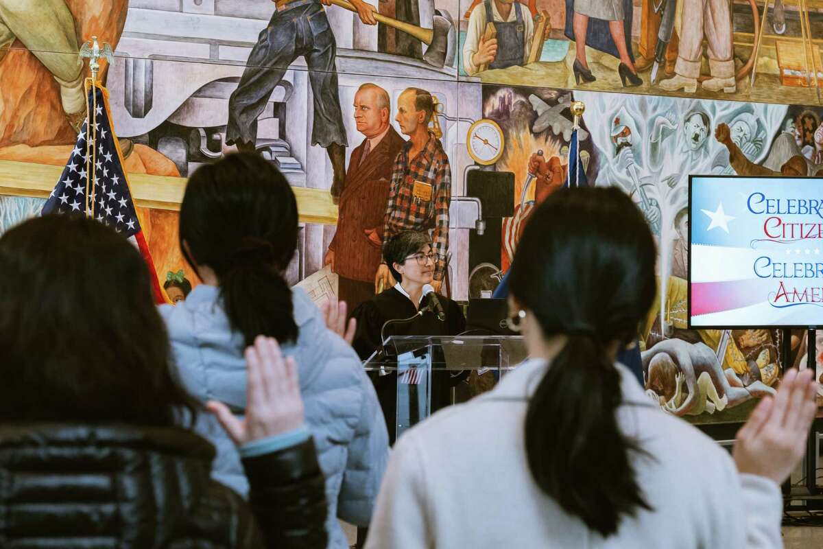 Judge Lisa Cisneros leads the Oath of Allegiance in front of Diego Rivera’s “Pan American Unity” fresco at the San Francisco Museum of Modern Art.
