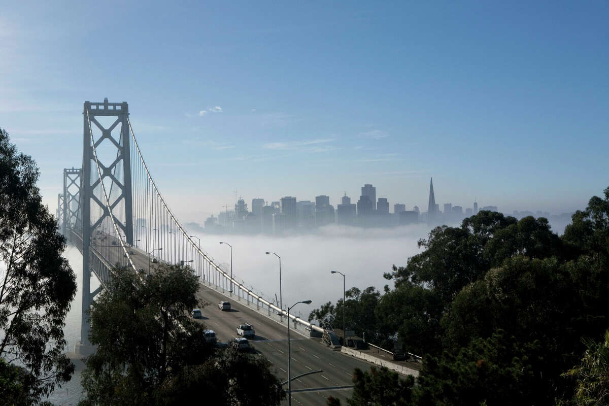 Skyline of San Francisco peeks out from a heavy fog, as seen from the Yerba Buena Island overlooking the Bay Bridge in San Francisco, Calif.