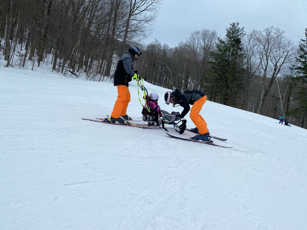 Amira Dorval, who is 5, lost her boot in the excitement of skiing Upper Whirlaway at Jiminy Peak in Hancock, Mass. STRIDE volunteer Renee South puts it back on while Rich Peters holds the tethers.