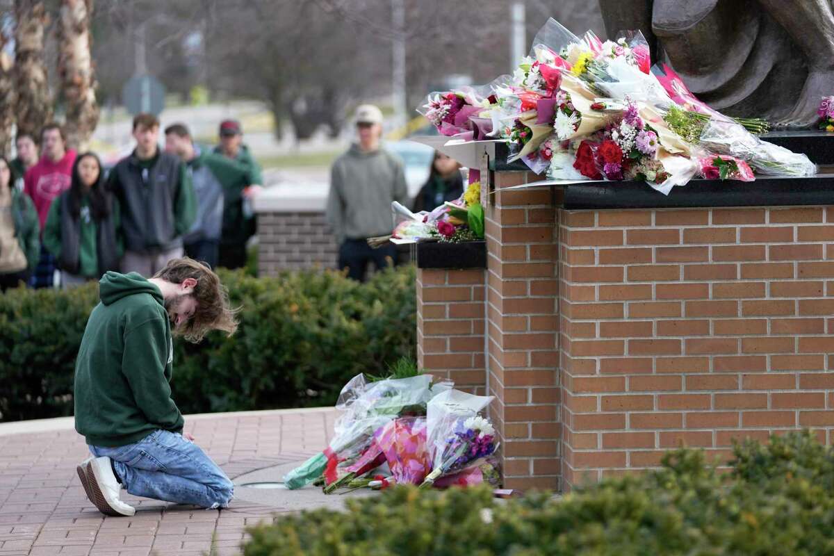A student kneels where flowers are being left at the Spartan Statue on the grounds of Michigan State University, in East Lansing, Mich., Tuesday, Feb. 14, 2023. A gunman killed several people and wounded others at Michigan State University. Police said early Tuesday that the shooter eventually killed himself.