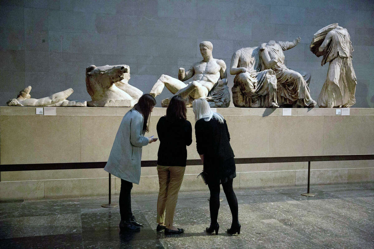 Women at The British Museum stand by a marble statue from the east pediment of the Parthenon. The chairman of the British Museum said the U.K. and Greece are working on a deal that would see the Parthenon Marbles displayed in both London and Athens.