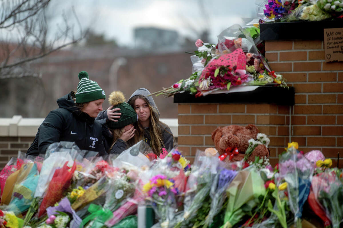 Michigan State University freshmen McKenzie English and Carolina Gorinkowski, both 18, console one another alongside Alyssa Pollard-McGrandy, a doctoral candidate in MSU's kinesiology department, as the trio lay flowers at the foot of the Spartan Statue where a makeshift memorial continues to grow after three students were shot and killed Feb. 13. Five others were also injured. 