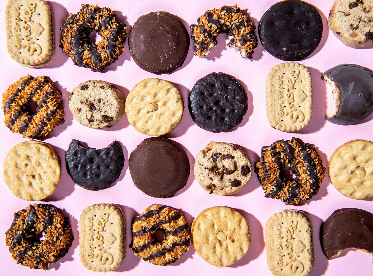 An array of Girl Scout Cookies are shown against a pink background. The sale of the treats is a cherished American tradition.