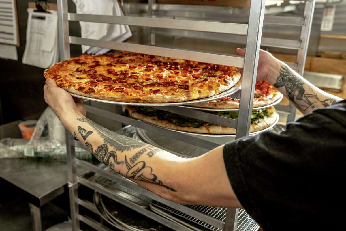 Eric Ehler, co-owner of Outta Sight Pizza in San Francisco, places a freshly baked pizza onto a rack. His restaurant opening defied a slowdown in the Tenderloin last year.