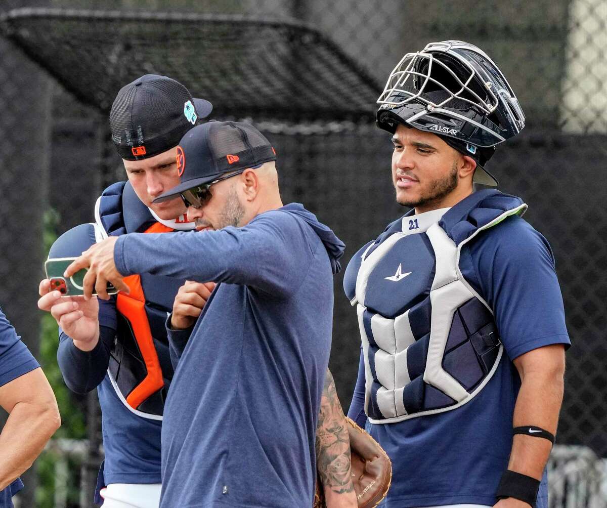 Houston Astros bullpen catcher Javier Bracamonte (85) shows catchers Korey Lee and Yainer Diaz a video. Lee and Diaz are competing for roster spot as backup backstop.